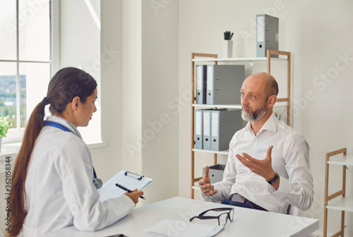 Male patient pensioner speaks with the doctor at the desk in the office of the hospital.