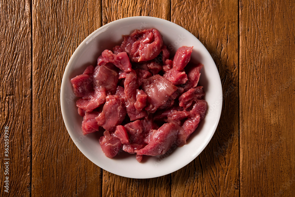 White bowl with meat raw on wood background. Top view.