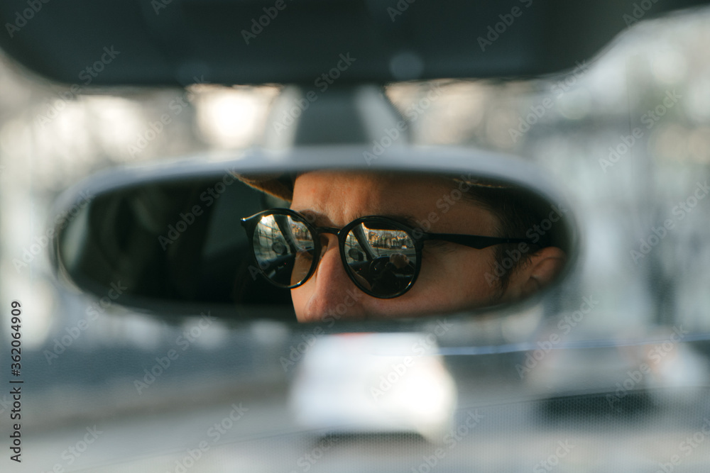 man wearing glasses behind the wheel of a car in reflection