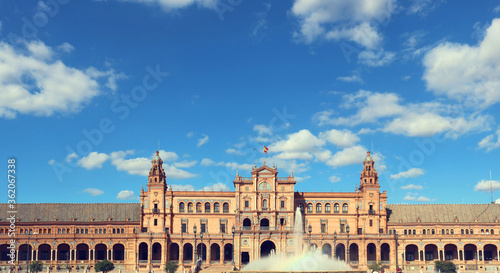 main building of plaza de espana in seville, with the monument palace, the fountain and a blue sky with clouds in the background - horizontal postcard or wallpaper