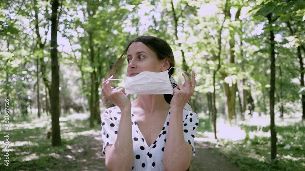 Young woman removes mask while nobody sees and puts on, she makes breath of fresh air in Park. concept of removing limitations of pandemic or end of Allergy Young woman removes mask while nobody sees and puts on, she makes breath of fresh air in Park. concept of removing limitations of pandemic or end of Allergy