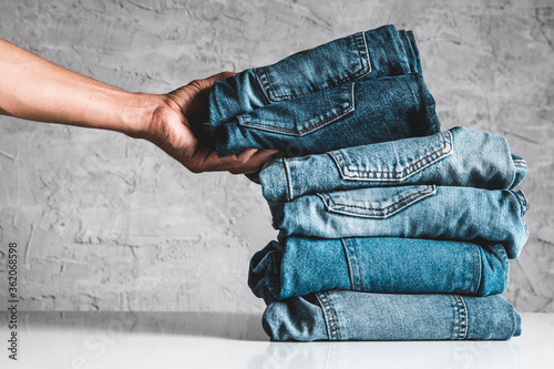 Hands, put the stack of blue jeans on gray background.