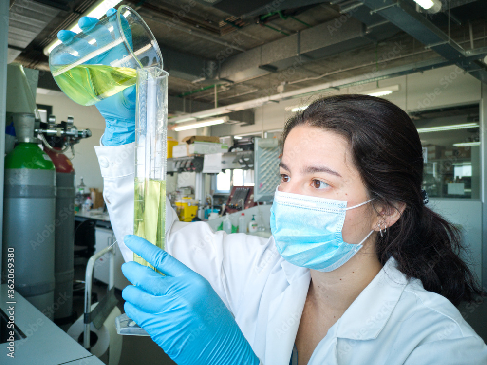 Young female lab technician making up to volume with yellow liquid into a measuring cylinder. Researcher and laboratory concepts. Young female lab technician making up to volume with yellow liquid into a measuring cylinder. Researcher and laboratory concepts.