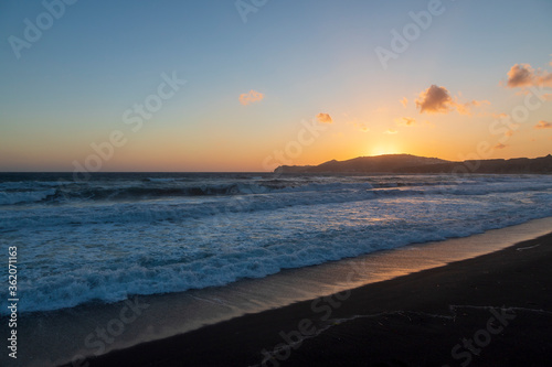 Beautiful coast at sunrise Vlychada beach on Santorini island in Greece. On the background of the sea is a blue sky with the rising sun.
