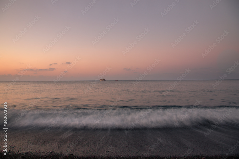 Perivolos beach on Santorini island in Greece at sunrise. The background is a blue sky with white clouds.