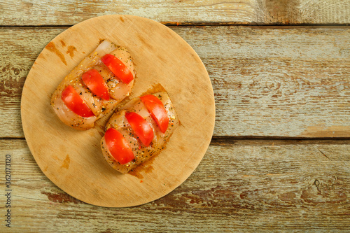 Chicken breast in marinade stuffed with tomatoes on a round wooden board. Copy space.