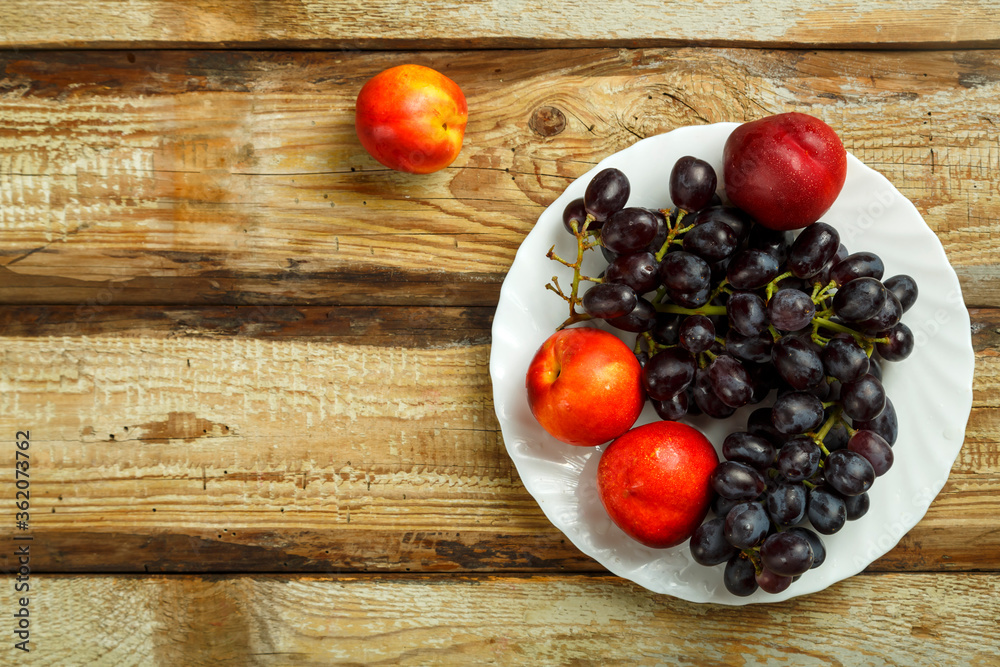 Grapes and peaches on a white plate on the table. Copy space. Grapes and peaches on a white plate on the table. Copy space.