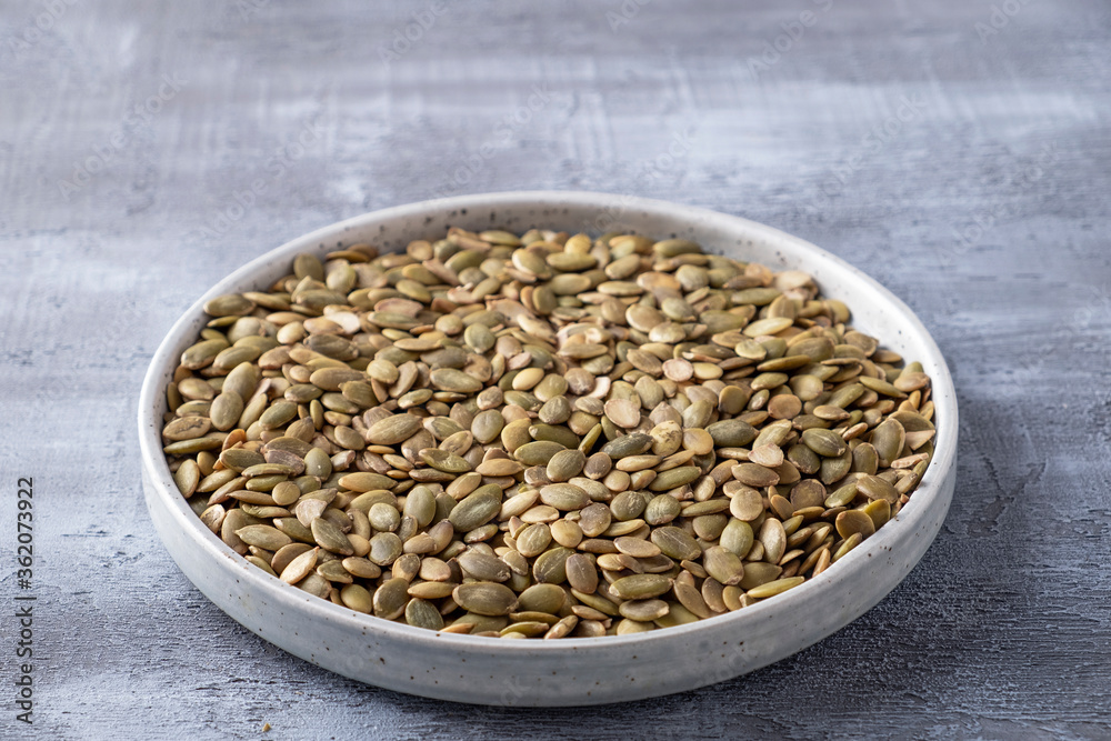 Raw pumpkin seeds in a plate on grey backgrouns. Superfood