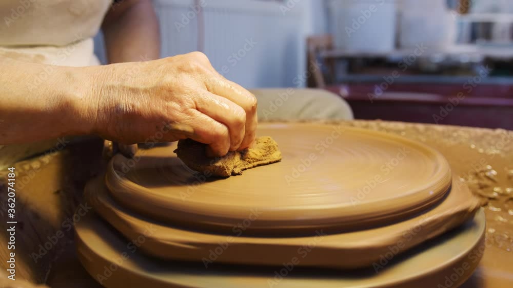 Close up of male potter shaping clay for plate on pottery wheel in ceramics studio - shot in slow motion Close up of male potter shaping clay for plate on pottery wheel in ceramics studio - shot in slow motion