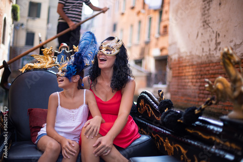A mother is having fun with her daughter on gondola at Venice, Italy. Venetian mask and family concept.