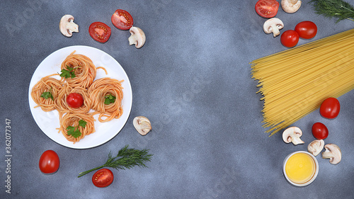 Italian pasta spaghetti and ingredients for cooking, cherry tomatoes, olive oil and spices on a dark table, top view, place for text