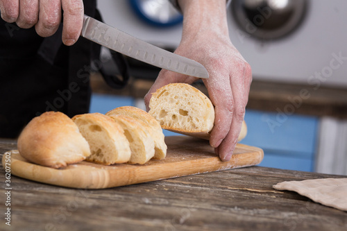 Striped baguette on a board. The knife is in men's hands. Kitchen view 