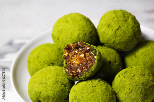 Homemade energy balls with dried apricots, raisins, dates, prunes, walnuts, pistachios and green matcha. Healthy sweet food. Energy balls in a plate on a marble grey background. Close up. Side view.