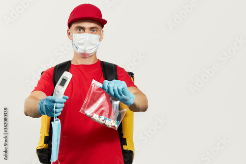 A courier in a red uniform, protective mask and gloves delivers pill drug and thermometer. Stay at home and take care of your health. Courier drug delivery photo