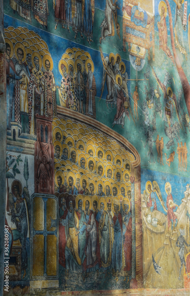 VORONET MONASTERY, BUCOVINA, ROMANIA, EUROPE, SPRING 2018. Back of the Orthodox Voronet Monastery with outdoor paintings and portraits of Byzantine-influenced saints. Moldovan architectural style.