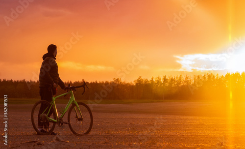 Man with a gravel bike stands in a field on a beautiful sunset background.