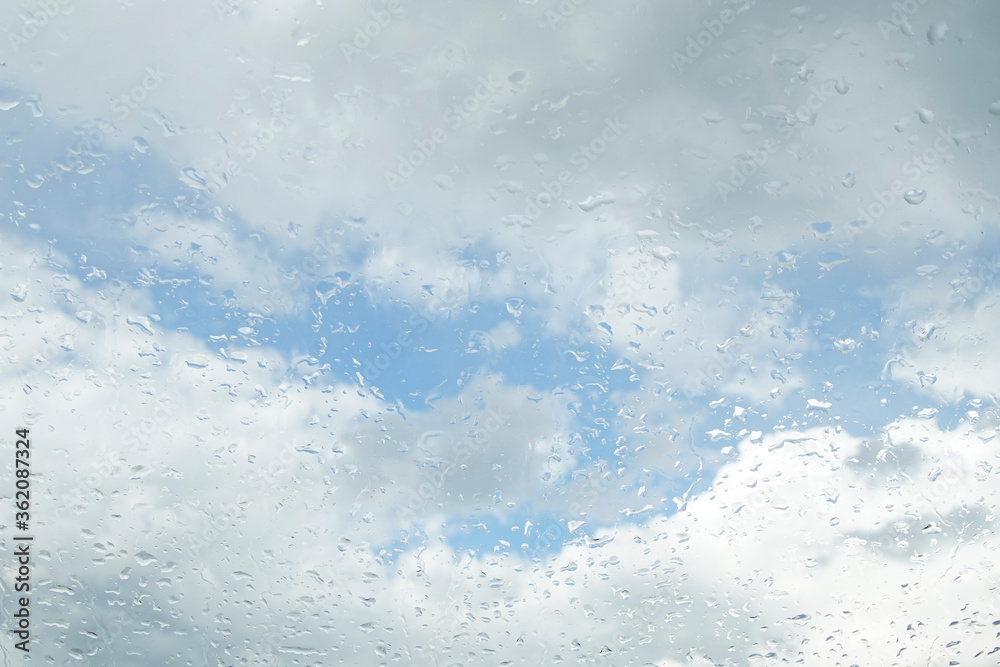 Fototapeta premium Raindrops on the window glass. Clear blue sky with white clouds. Blurred background.