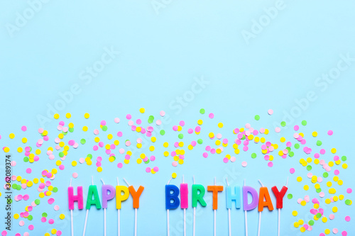 Happy birthday candles and confetti on blue background, to view