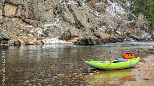 inflatable whitewater kayak with a paddle and dry bag on a rocky shore of a mountain river, early spring scenery - Poudre RIver at Picnic Rock above Fort Collins, Colorado
