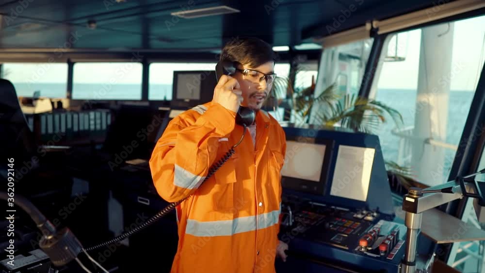 Filipino deck Officer on bridge of vessel or ship wearing coverall during navigaton watch at sea . He is speaking on GMDSS VHF radio, communication between vessels. Filipino deck Officer on bridge of vessel or ship wearing coverall during navigaton watch at sea . He is speaking on GMDSS VHF radio, communication between vessels.