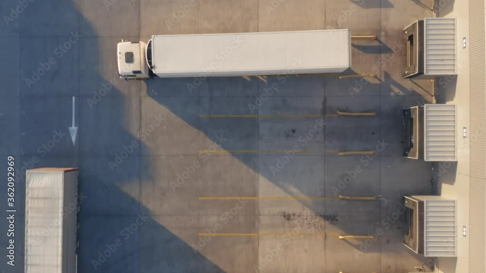 Aerial top down view of a lot of semi trucks with cargo trailers awaiting for loading/unloading goods on ramps on the big logistics park (loading hub) with warehouse. Aerial top down view of a lot of semi trucks with cargo trailers awaiting for loading/unloading goods on ramps on the big logistics park (loading hub) with warehouse.