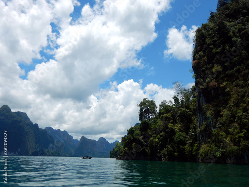 Lush forest on the lake's edge. Blue sky with scattered cloud in Khao Sok National Park.