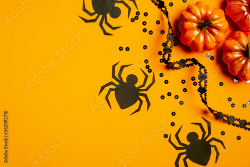 Halloween party concept. Flat lay composition with pumpkins  black spiders  confetti  ribbon on orange background. Top view  overhead.