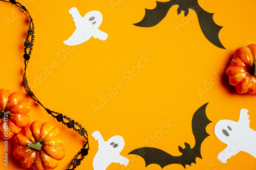 Halloween concept with pumpkins, bats, ghosts, black ribbon on orange background. Halloween banner template, flat lay, top view.