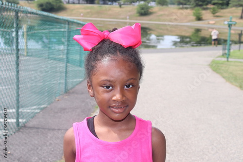 Token Black Girl wearing Pink sleeveless shirt with pink hair bow in suburban park photo