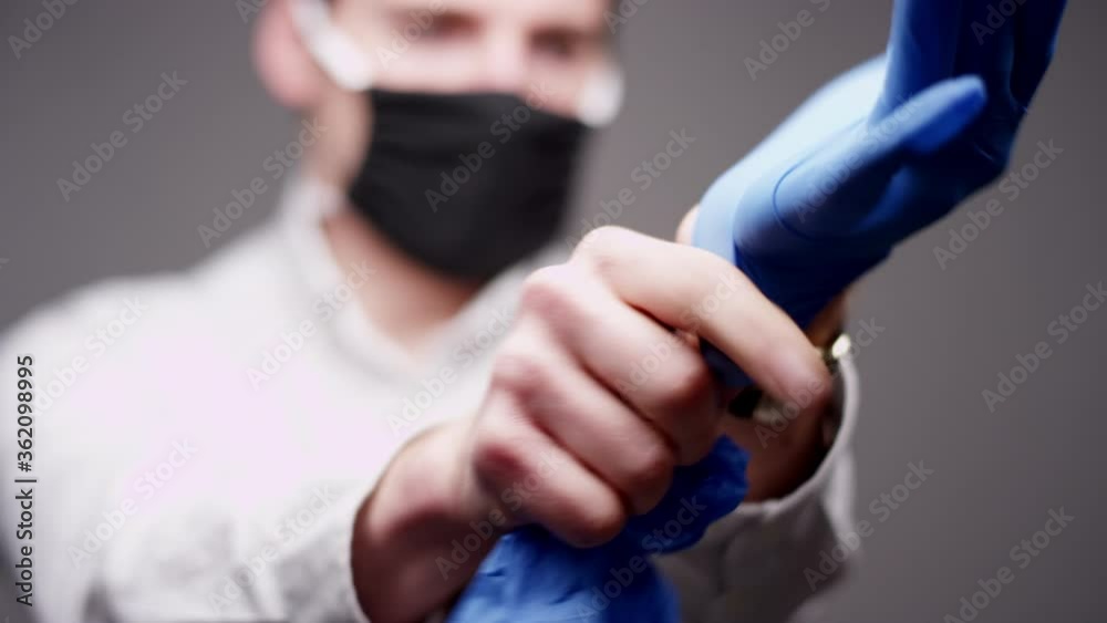 Man wearing a face mask puts on blue latex gloves to protect from coronavirus Man wearing a face mask puts on blue latex gloves to protect from coronavirus
