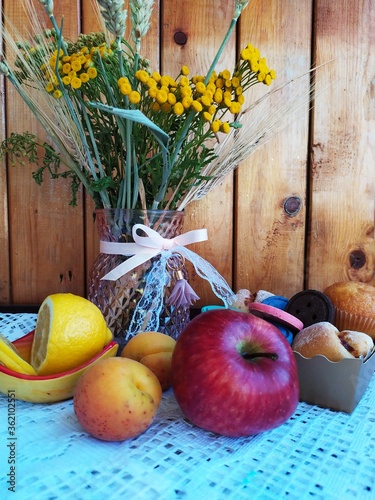 Food still life on the kitchen table a vase of wild flowers apples apricots sponge cakes lemon orange cookies in a basket