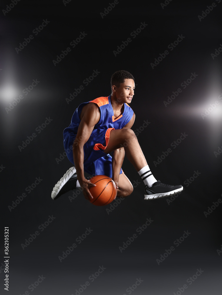 Young jumping African-American basketball player on dark background