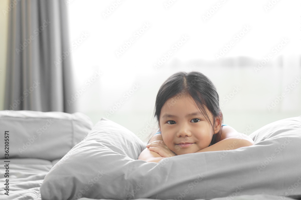 Asian child smile or kid girl happy lie down or sleep on soft pillow to comfortable on gray bed relax and white curtain with window light and stay home safe in morning to wake up or woke up at bedroom Asian child smile or kid girl happy lie down or sleep on soft pillow to comfortable on gray bed relax and white curtain with window light and stay home safe in morning to wake up or woke up at bedroom