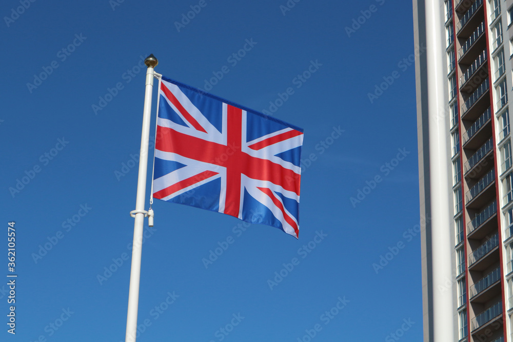 The flag of Great Britain against the blue sky near the multi-storey residential building.