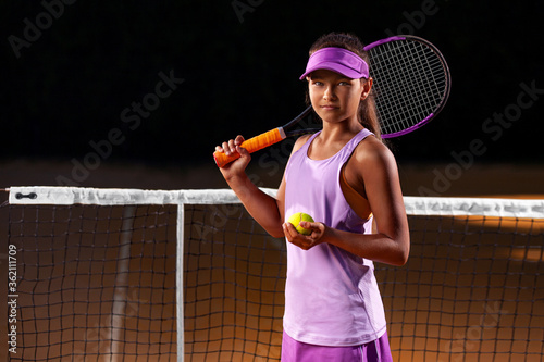 Portrait of kid - tennis player. Beautiful girl athlete with racket in pink sporswear and hat on tennis court. Fashion and sport concept. photo