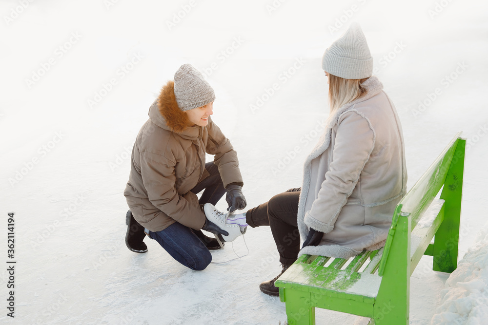 Man helps to put on skates for ice rink snow to girl, concept of winter vacation, family rest