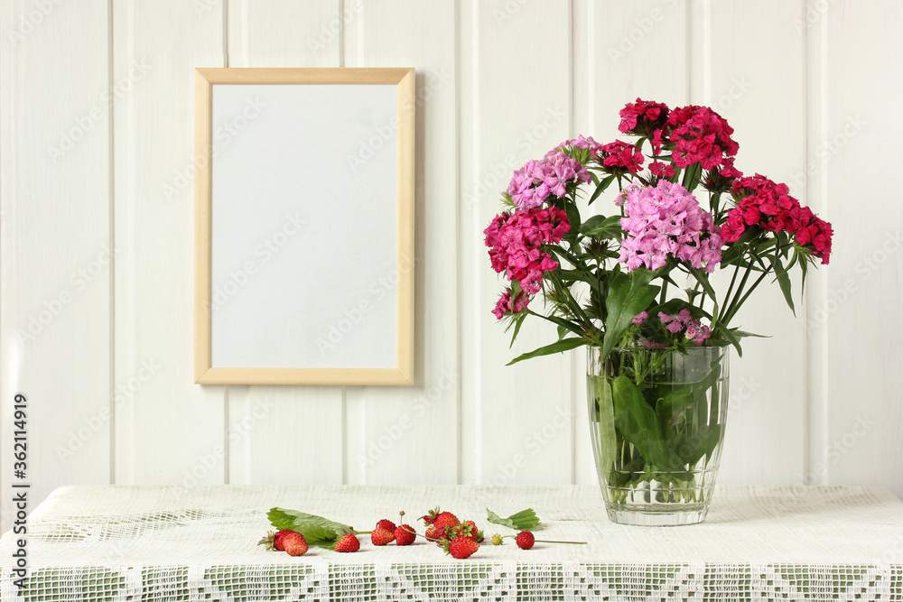 empty frame on the wall, bouquet of Turkish carnations and garden strawberries. empty frame on the wall, bouquet of Turkish carnations and garden strawberries.