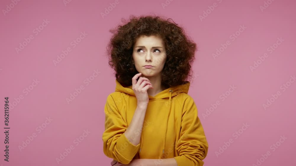 Thoughtful confused girl afro hairstyle in hoodie touching chin, scratching head while thinking over solution, having doubts about difficult choice. indoor studio shot isolated on pink background Thoughtful confused girl afro hairstyle in hoodie touching chin, scratching head while thinking over solution, having doubts about difficult choice. indoor studio shot isolated on pink background
