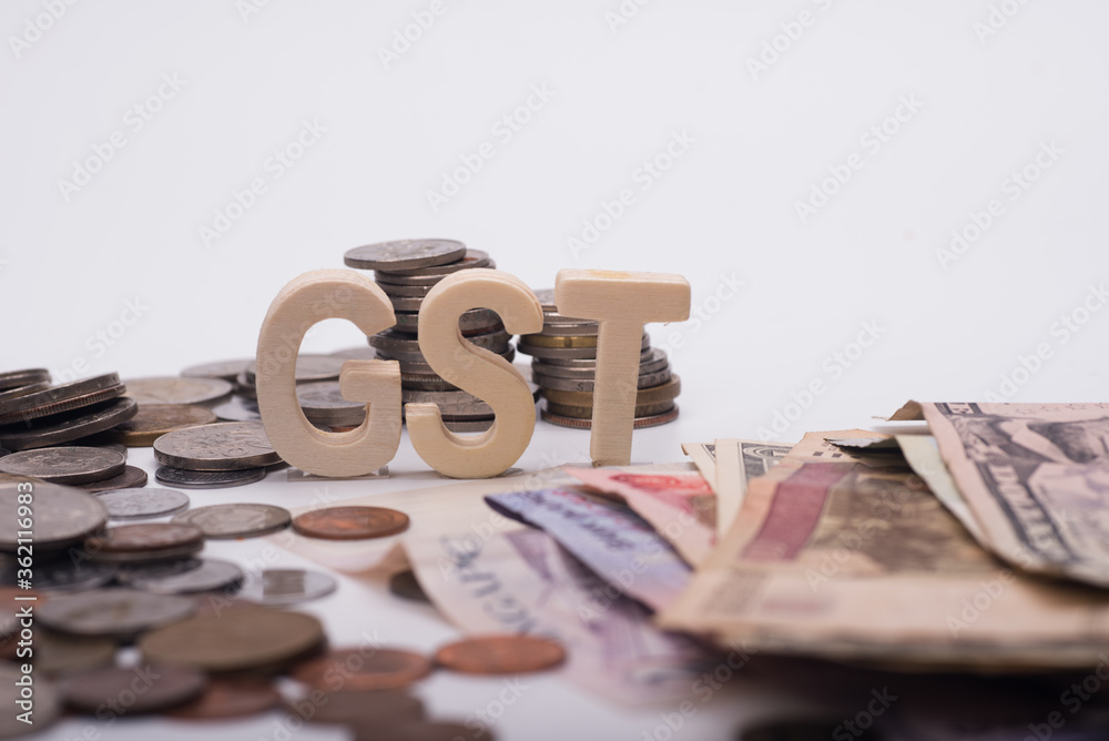 GST wooden alphabet over spread of bank notes and coins over white