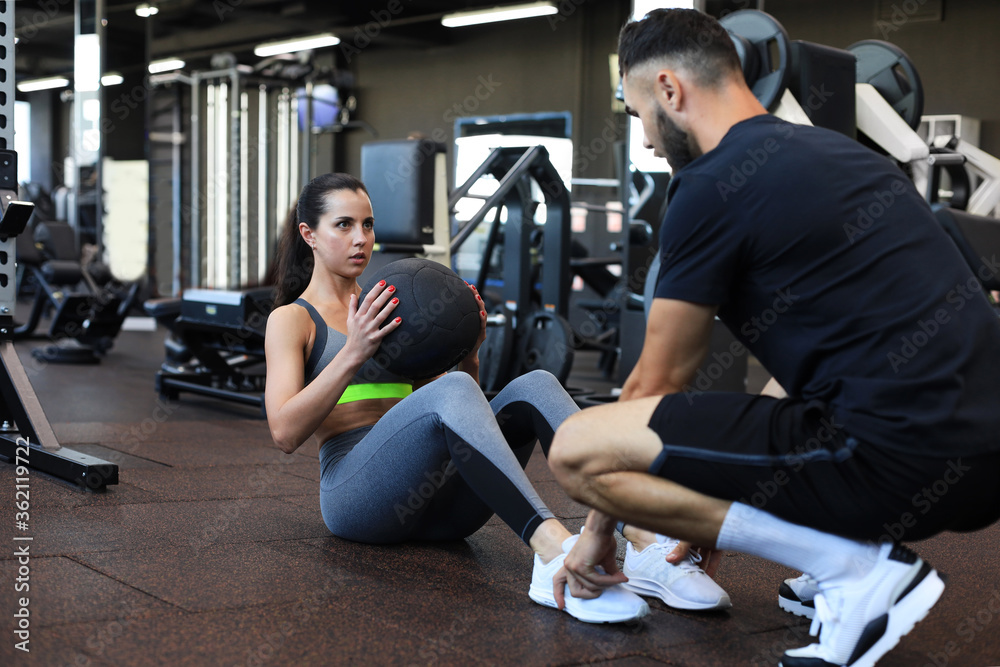 Obraz premium Trainer helping young woman to do abdominal exercises in gym.