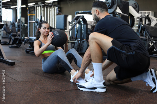 Fototapeta Naklejka Na Ścianę i Meble -  Trainer helping young woman to do abdominal exercises in gym.