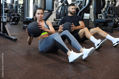 Beautiful young sports couple is working out with medicine ball in gym.