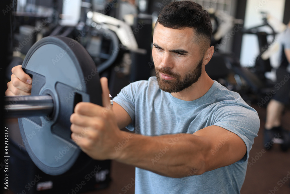 Muscular sporty indian man adding weight on barbell at gym. Muscular sporty indian man adding weight on barbell at gym.