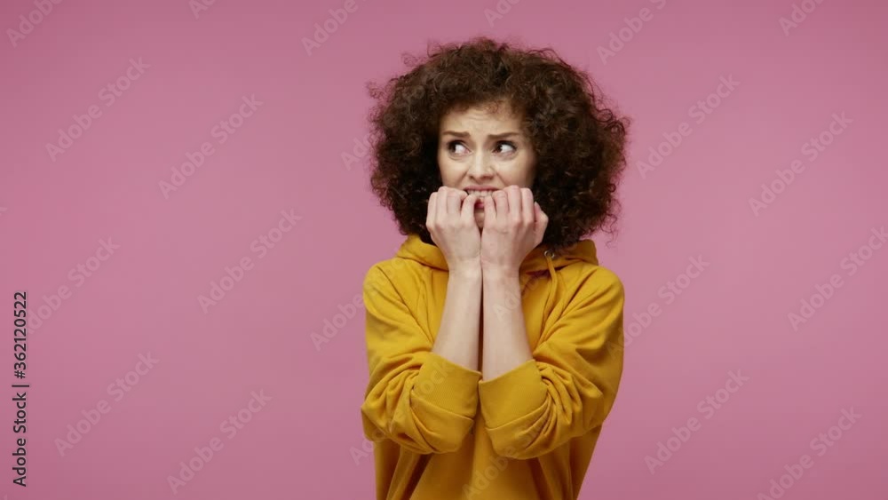 Insecure frightened girl afro hairstyle in hoodie biting nails, feeling worried nervous about serious troubles, stress and anxiety disorder concept. indoor studio shot isolated on pink background Insecure frightened girl afro hairstyle in hoodie biting nails, feeling worried nervous about serious troubles, stress and anxiety disorder concept. indoor studio shot isolated on pink background