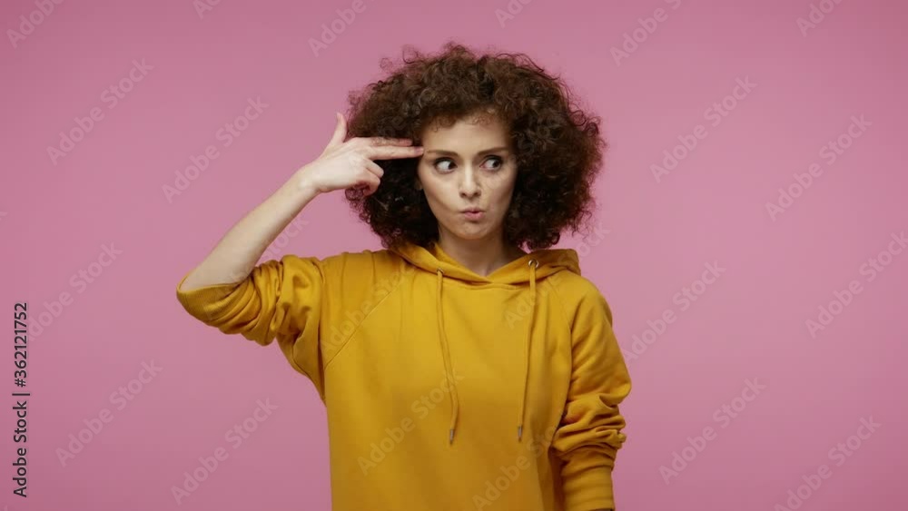 Suicide gesture. Depressed girl afro hairstyle in hoodie aiming finger gun to head, shooting killing herself, pretending to die with crossed eyes and tongue out. indoor studio shot isolated on pink Suicide gesture. Depressed girl afro hairstyle in hoodie aiming finger gun to head, shooting killing herself, pretending to die with crossed eyes and tongue out. indoor studio shot isolated on pink