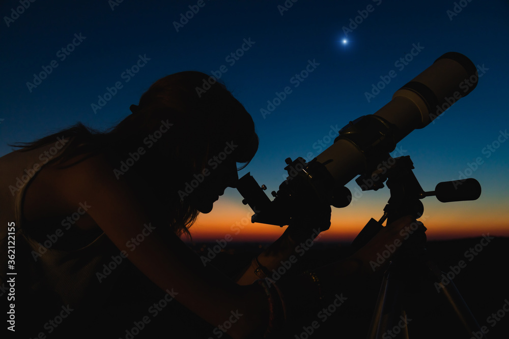 Silhouette of a woman and telescope with twilight sky.