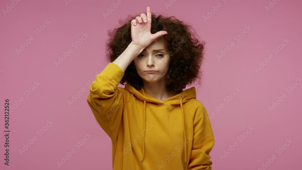 Unlucky sad girl afro hairstyle in hoodie showing loser or lame gesture, L finger sign on forehead, life troubles and unemployment concept, fired from job. studio shot isolated on pink background Unlucky sad girl afro hairstyle in hoodie showing loser or lame gesture, L finger sign on forehead, life troubles and unemployment concept, fired from job. studio shot isolated on pink background