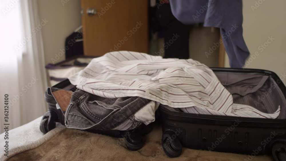 Man throwing clothes from his closet into a suitcase on the bed Man throwing clothes from his closet into a suitcase on the bed