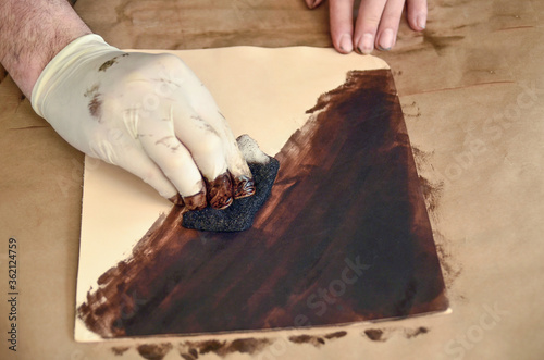 Colouring cowhide slice. Handbag making process. Colorings piece of buff with brown color. Male hand with tampon photo