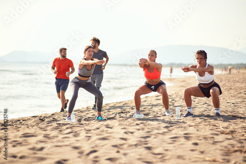 group of three women exercise on a beach while two men passing by, jogging